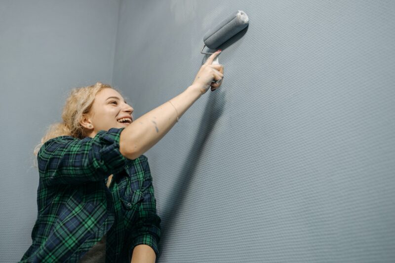 Giving your walls a fresh new look is a great way to update your home decor on a budget. image - A smiling woman painting the walls grey.